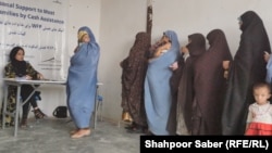یک کارمند زن برنامه جهانی غذا زنان بی‌بضاعت را در هرات برای دریافت کمک‌های بشری ثبت نام می‌کند. عکس از آرشیف