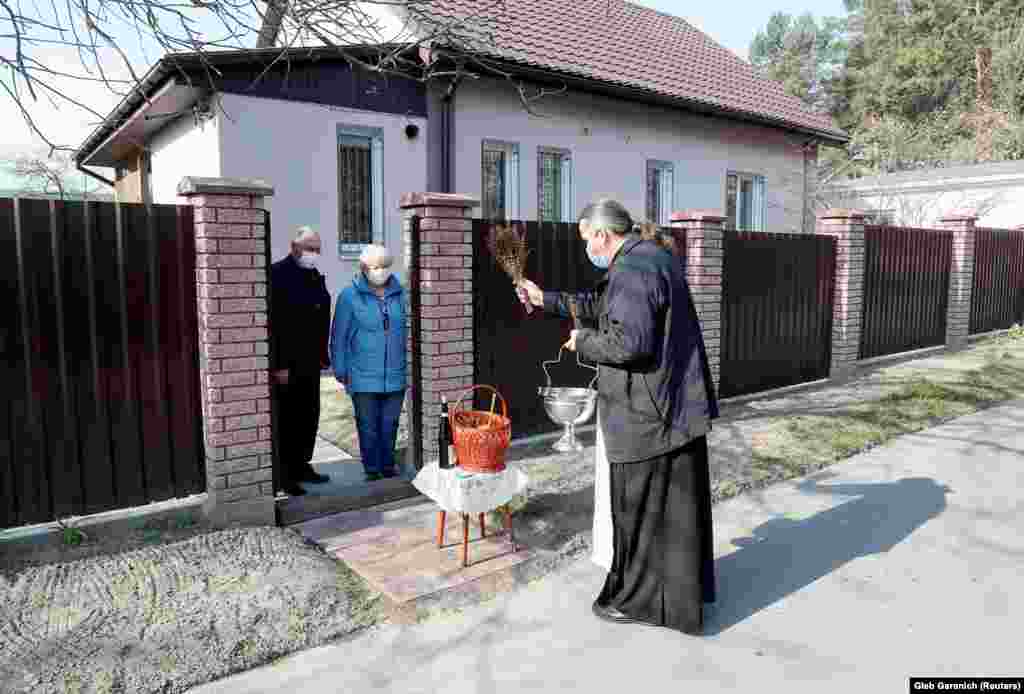 Православный священник, соблюдая социальную дистанцию, освящает пасхальные куличи и яйца для пожилой пары в поселке недалеко от Киева, Украина, 19 апреля 2020 года. 