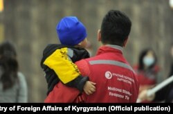 Қызыл жарты ай ұйымының қызметкері Ирактан Қырғызстанға жеткізілген баланы көтеріп тұр.