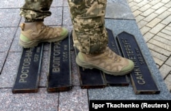 Украинский военнослужащий стоит на табличках с названиями городов России (Ростов-на-Дону, Волгоград, Таганрог, Москва и Санкт-Петербург) после того, как они были демонтированы с декоративного уличного знака в Одессе, что указывает направления и расстояния до ряда городов. Одесса, 14 апреля 2022 года.