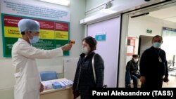 Медработник замеряет температуру тела посетителя больницы.