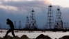 Рабочий на фоне нефтяных вышек на берегу Каспийского моря. 